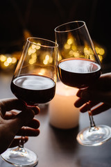 Two glasses of wine  red in hand on the background candle and  garlands 