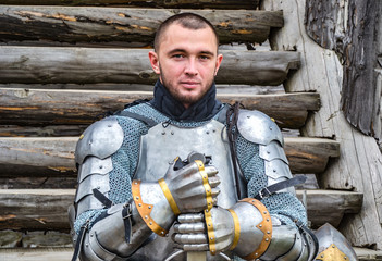 Knight in the armor on the wooden steps. Knightly armor and weapon. Semi - antique photo.