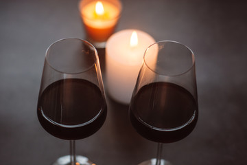 Two glasses of wine  red standing on a dark table with candle and  garlands