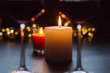 Two candles are on a dark table on the background of the garlands