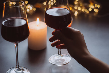 Two glasses of wine  red in hand on the background candle and  garlands 