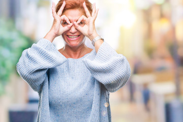 Atrractive senior caucasian redhead woman wearing winter sweater over isolated background doing ok gesture like binoculars sticking tongue out, eyes looking through fingers. Crazy expression.