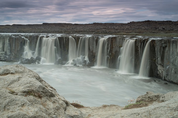 Obraz premium The Sellfoss Waterfall with golden clouds in the sky. The flowing water is captured by a long exposure. Amazing blue color of water from the glacier. Natural and colorful environment. Iceland..