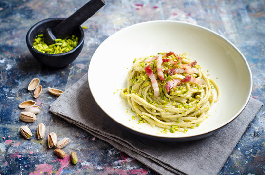 Bowl of spaghetti pasta with pistachio pesto and crispy pork cheeck guanciale and pancetta bacon in a white bowl