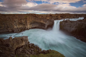 The waterfall Aldeyjarfoss with golden clouds in the sky. The flowing water is captured by a long...