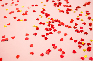 Defocused and blurred beautiful heart and stars shaped red confetti on pink background.