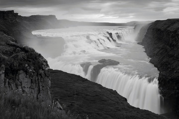 The Gullfoss Waterfall with golden clouds in the sky. The flowing water is captured by a long exposure. Amazing blue color of water from the glacier. Natural and colorful environment...