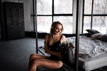 A beautiful blonde in a black body posing at a metal black bed.