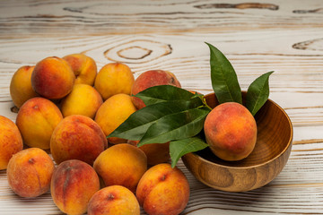 ripe peaches in a wooden plate with leaves on the table