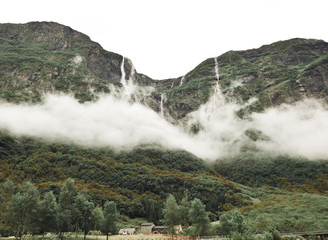 Fototapeta na wymiar Clouds form moody cloaks around the high waterfalls of Norwegian fjords 