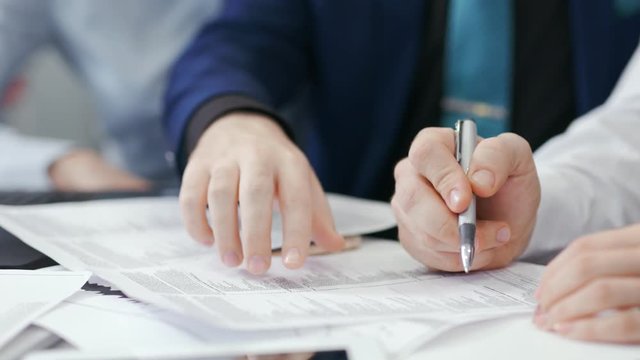 Close-up hands of two businessman during team meeting holding pen showing details at paper document
