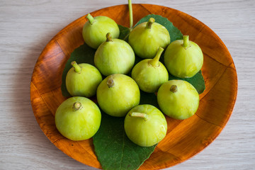 Green figs on a leaf in a wooden tray