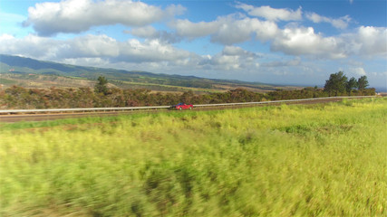 AERIAL: Red convertible driving on countryside road along the canyon in Hawaii