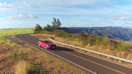 AERIAL: Red convertible sportscar driving along majestic Waimea canyon landscape