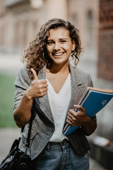 Portrait of a smiling female mixed race student showing thumb up outdoors