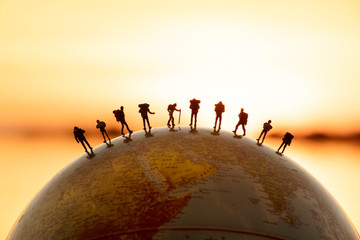 miniature figure people backpack standing on globe with sunset or sunrise sky background