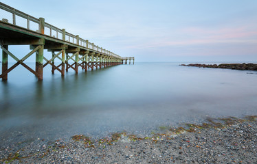 Obraz premium Overview of beautiful fishing pier after sunset at low tide at Walnut Beach, Milford Connecticut, USA.