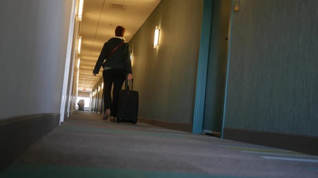 Woman walks down modern hotel hallway with luggage bag