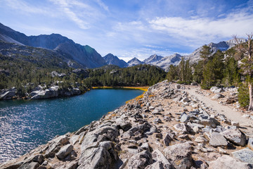 Hiking trail following the shoreline of an alpine lake surrounded by the rocky ridges of the Eastern Sierra mountains; Box Lake, Little Lakes Valley trail, John Muir wilderness, California