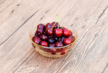 Berries of a sweet cherry in a glass bowl on a wooden background. Ripe red sweet cherry.