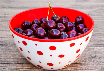 Berries of a sweet cherry on a wooden background in a plastic cup. Ripe red sweet cherry.