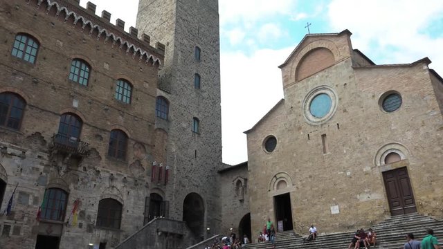 Tourists walking around Duomo and medieval towers. People on vacation visiting cathedral and buildings. Italian attraction, sightseeing, tourism destination. San Gimignano, Tuscany, Italy
