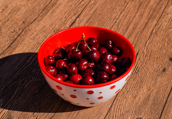 Berries of a sweet cherry on a wooden background in a plastic cup. Ripe red sweet cherry.