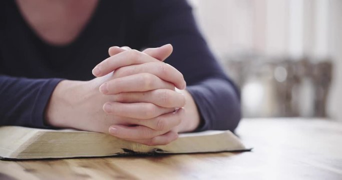 Christianity and faith concept - a handheld closeup shot of a woman praying over an open Bible at home.