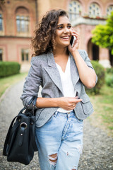 Young mixed race woman university student talking on the phone in campus garden