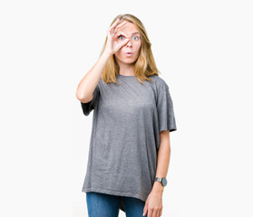 Fototapeta premium Beautiful young woman wearing oversize casual t-shirt over isolated background doing ok gesture shocked with surprised face, eye looking through fingers. Unbelieving expression.