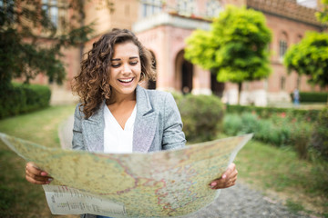 Happy female tourist exploring map while standing in alley near vintage building. Trendy woman...