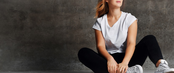 cropped shot of girl in jeans sitting on floor near grey wall