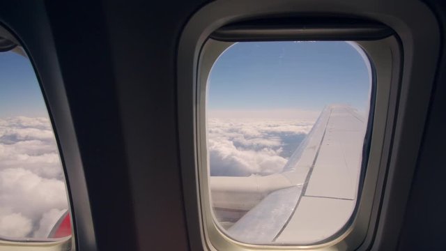A view through the windows of an airplane in flight with blue sky and white clouds in the distance.