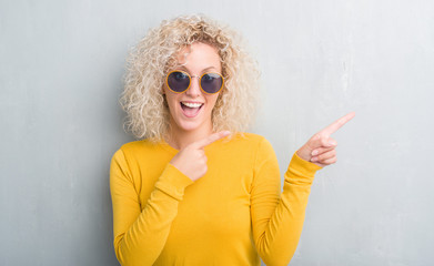 Young blonde woman with curly hair over grunge grey background amazed and smiling to the camera while presenting with hand and pointing with finger.