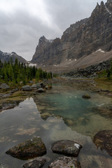 A shallow blue and orange colored alpine lake in a hanging valley of the rocky mountains reflects the surrounding landscape