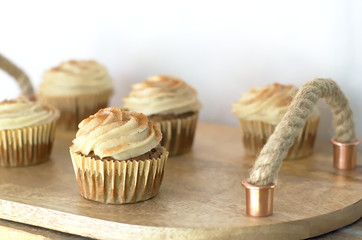 Chai-infused cupcakes with vanilla frosting on a wooden display tray