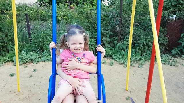 two sisters ride on children's swings. happy childhood in summer.