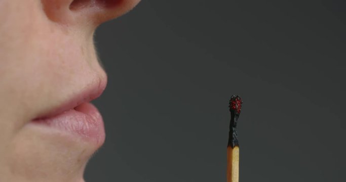 Closeup slow motion shot of a woman blowing a burning matchstick.