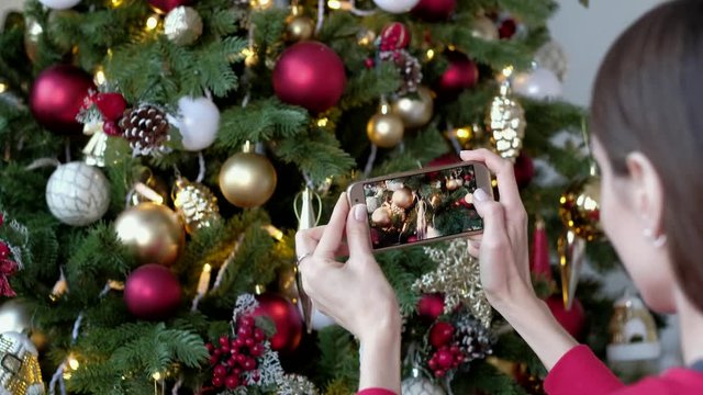 Female take photo on smartphone decorated christmas tree at home. X-mas, winter holidays and people concept.