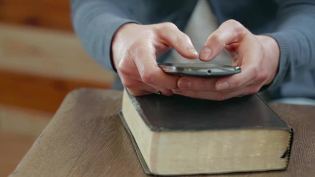 Young woman typing a text message or an e-mail on a smartphone over a Bible.