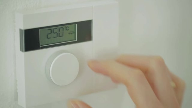 Female hand adjusting a room heating thermostat to 25 degrees Celsius.