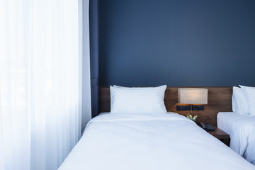 Close-up of white pillow on bed decoration with light lamp and digital telephone set in hotel bedroom interior.