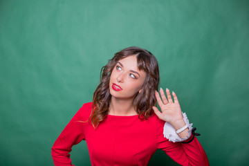 Gossip concept. Colorful studio portrait of pretty young woman with palm near her ear. pretty woman in red dress holds her hand near ear and listens isolated.Human face expression emotion reaction