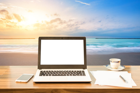 Mockup image of laptop with blank white screen,smart phone and document on wooden table at landscape early morning sunrise over the sea the horizon background. © Thinapob