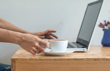 A Business woman is holding a white coffee cup during work with laptop-PC on office table