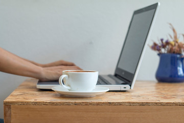A hot coffee cup on wooden table in coffee shop with person work online background, online work business concept