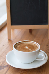 A white cup of hot coffee on wooden table,A refreshment before work time or refreshment in relaxing time in a break with empty black board for write menu in coffee shop
