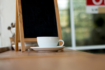 A white cup of hot coffee on wooden table,A refreshment before work time or refreshment in relaxing time in a break with empty black board for write menu in coffee shop