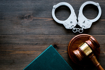 Crime concept. Metal handcuffs near judge gavel and law book on dark wooden background top view space for text