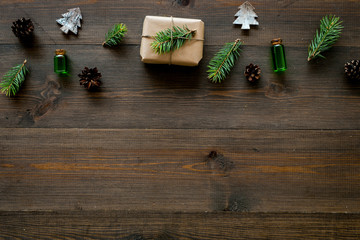 New Year pattern with pine sprigs, cones, spruce figure, fir oil and new year gift decorated with craft paper and pine sprout on dark wooden background top view copy space